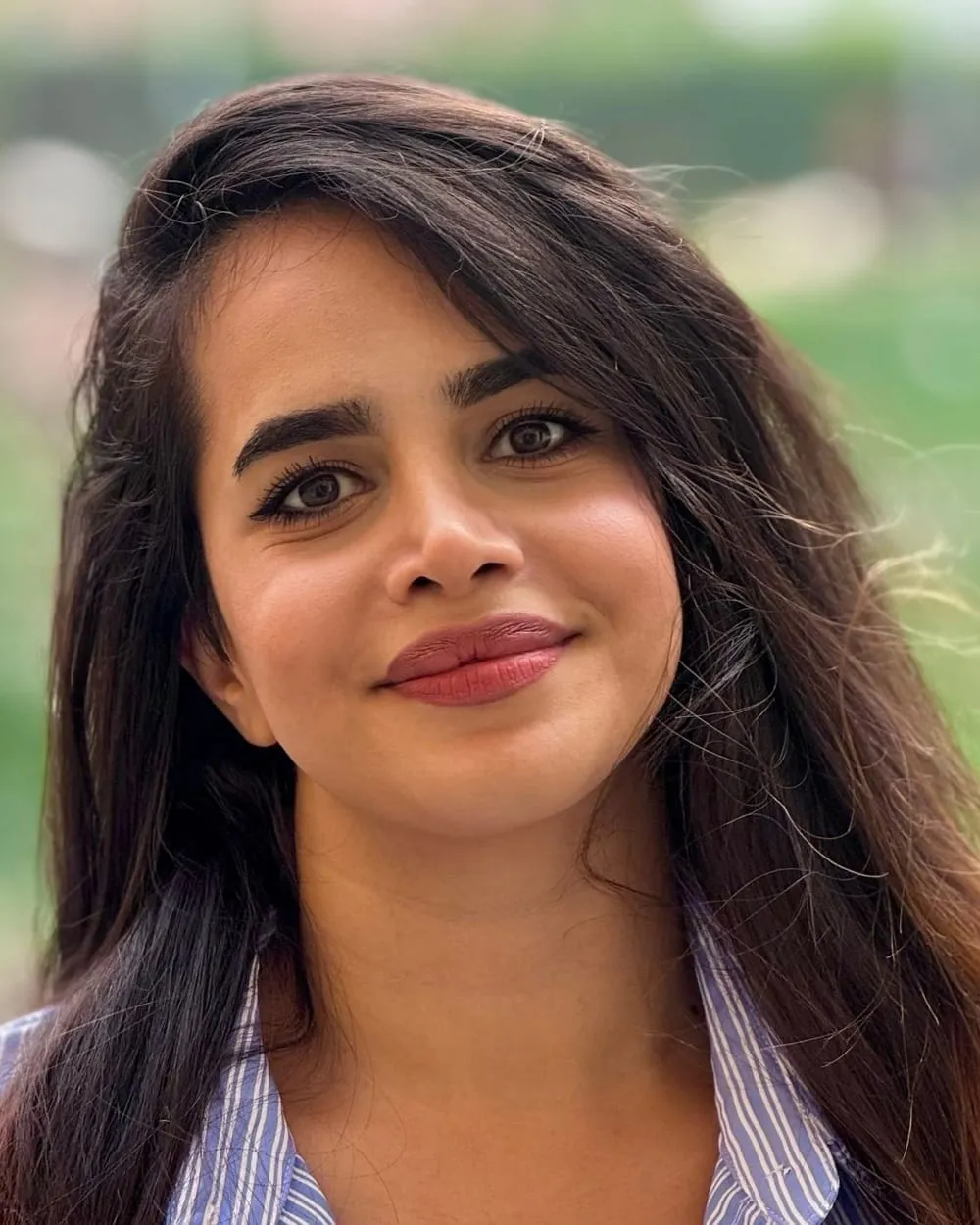 Neda smiling outdoors in a blue striped shirt